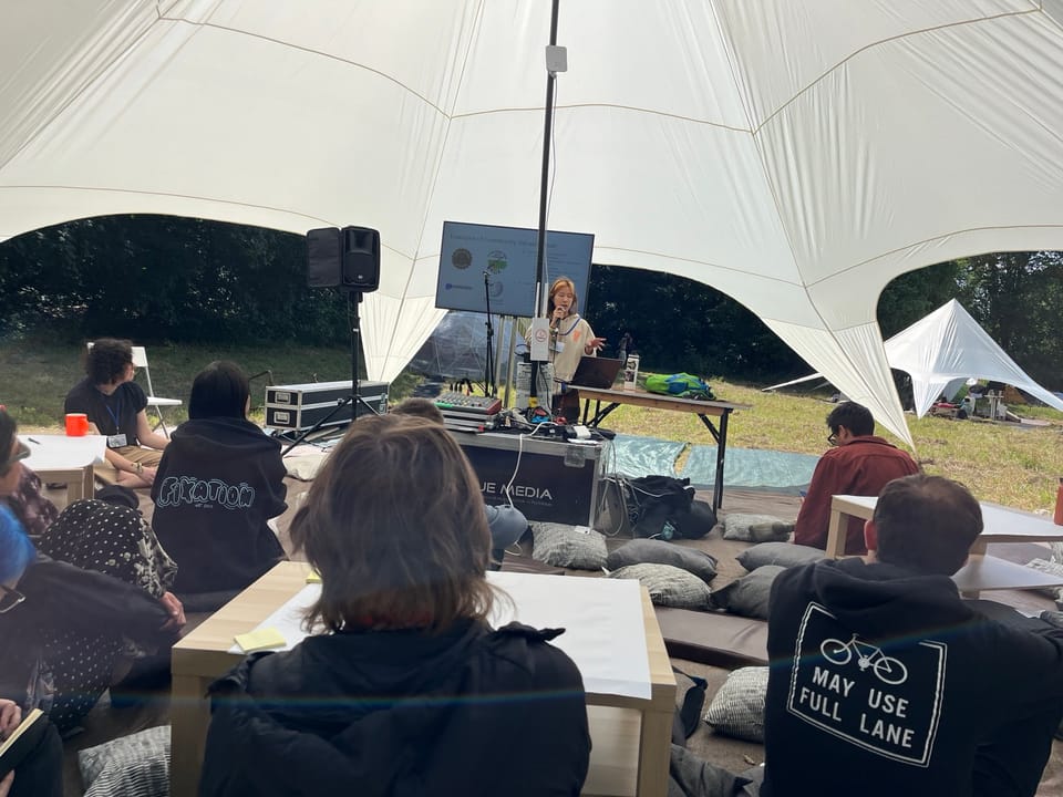 People in a large tent sitting on pillows watching a talk at DWeb Camp in Germany